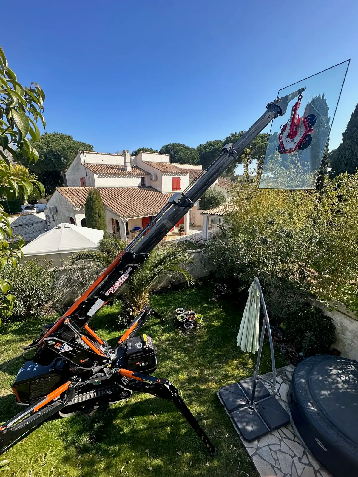 Mini-grue araignée levant un grand vitrage au-dessus d'un jardin, ciel bleu